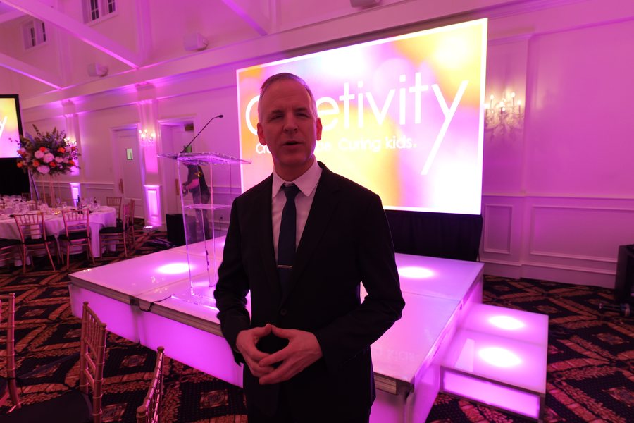 Speaker lit on an LED stage in front of the event screen at a charity gala produced by ATG