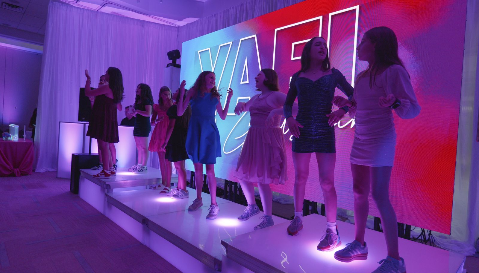Teens dancing on lit LED dance boxes in front of a custom name LED wall