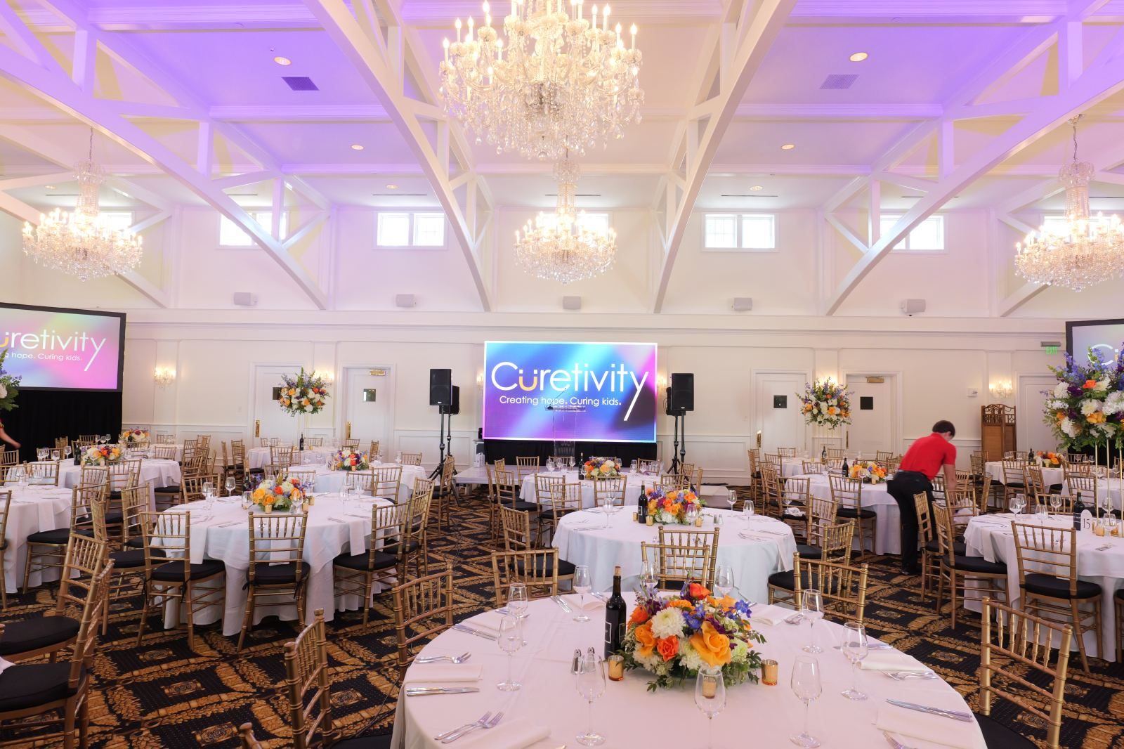 Gala ballroom with purple uplighting, chandeliers and two ATG video screens at Trump National Golf Club