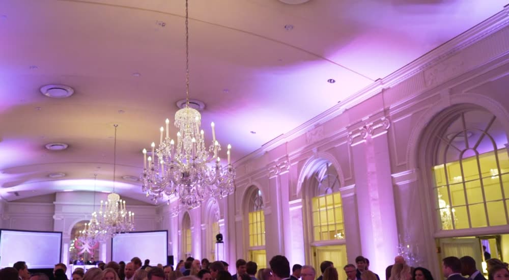 Chandelier ballroom with pink uplighting and screens set for a corporate event