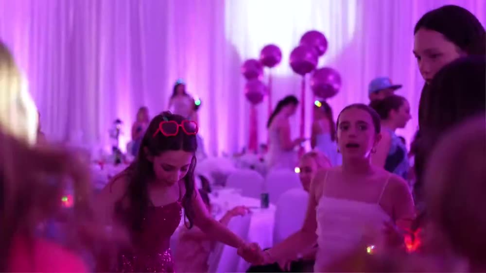 Teens dancing at a Bat Mitzvah with pink lighting and balloons