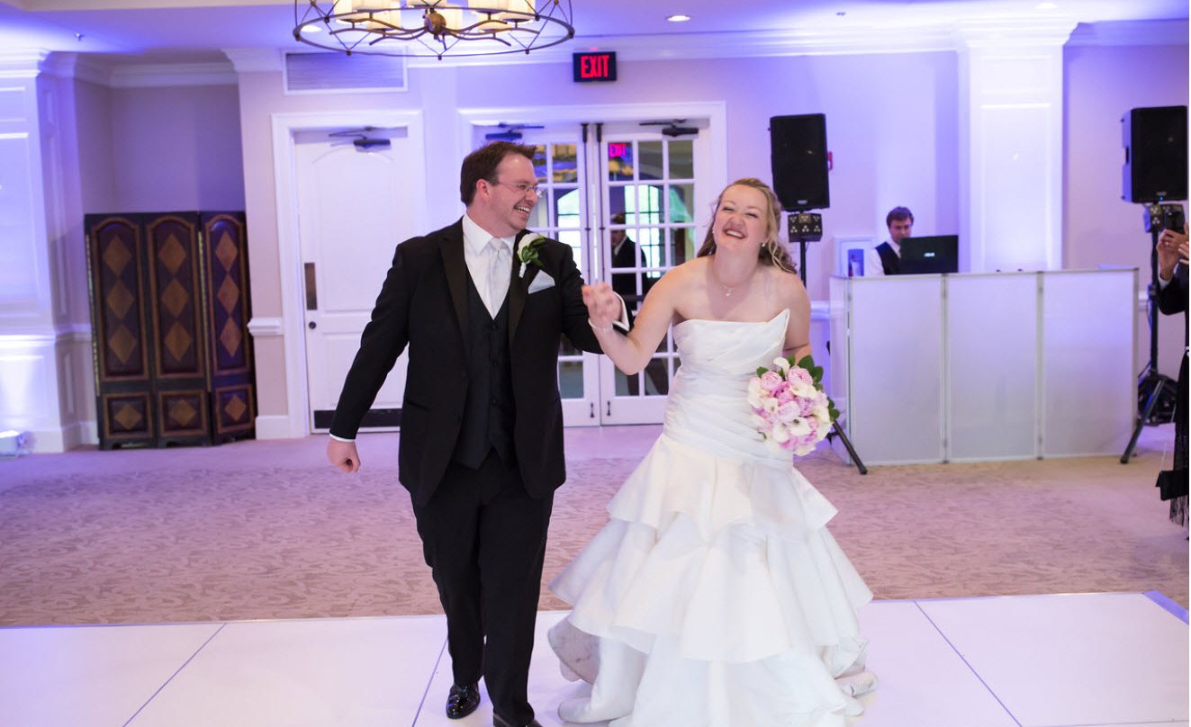 Bride and groom entering a reception past a white DJ booth
